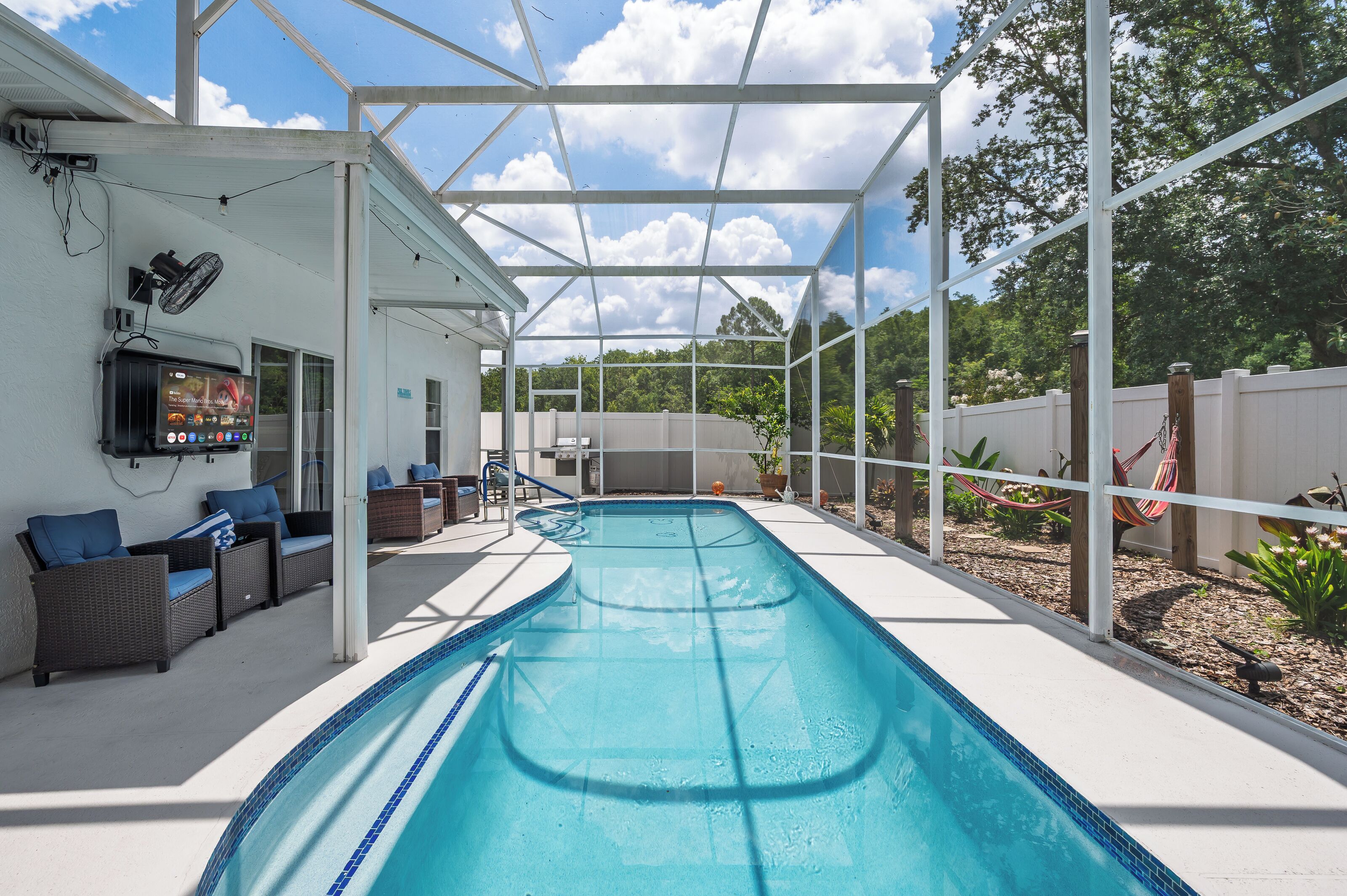 A covered outdoor swimming pool with lounge chairs and a television screen.