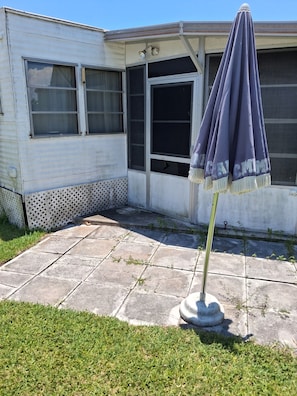 A white mobile home with a patio area, a window with a screen, and a purple umbrella. - Beautiful 1-bedroom mobile home with AC in Jensen Beach (Jensen Beach)