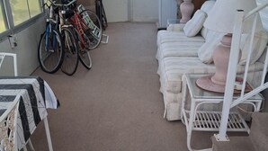A room with a carpeted floor, a sofa set, a table with a lamp, and bicycles parked against the wall. - Beautiful 1-bedroom mobile home with AC in Jensen Beach (Jensen Beach)