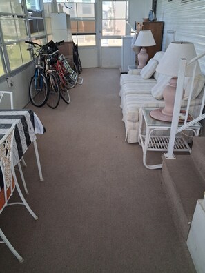 A room with a carpeted floor, a sofa set, a table with a lamp, and bicycles parked against the wall. - Beautiful 1-bedroom mobile home with AC in Jensen Beach (Jensen Beach)