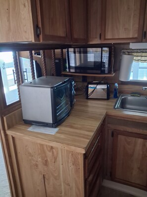 A compact kitchen with wooden cabinets, a microwave, a toaster, and a sink. - Beautiful 1-bedroom mobile home with AC in Jensen Beach (Jensen Beach)
