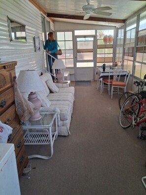 A room with a sofa set, a dining table, a bicycle, and a person standing by a window. - Beautiful 1-bedroom mobile home with AC in Jensen Beach (Jensen Beach)