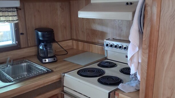 A kitchen with wooden cabinets, a white stove, a coffee maker, and a sink. - Beautiful 1-bedroom mobile home with AC in Jensen Beach (Jensen Beach)