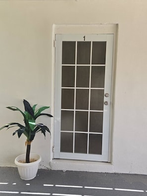 Eine weiße Tür mit Gittermuster und der Zahl 1, neben einem Blumentopf.