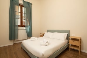 A bedroom with a bed, a nightstand, a window with curtains, and a radiator. - San Lorenzo Charming Apartment (Firenze)