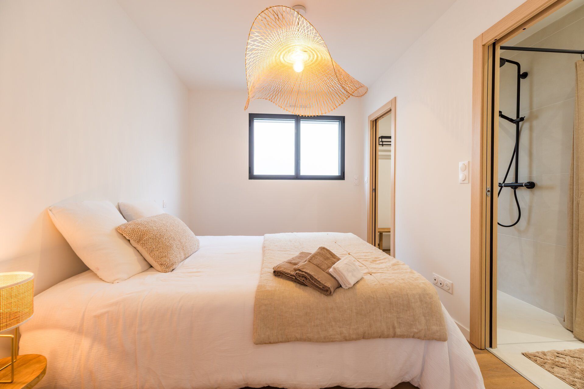 A bedroom with a bed, a hanging light fixture, a window, and a shower area.