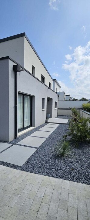 A modern building with a flat roof, large windows, and a paved walkway leading to a door. - Architect-designed house 800m from the sea (Paimpol)