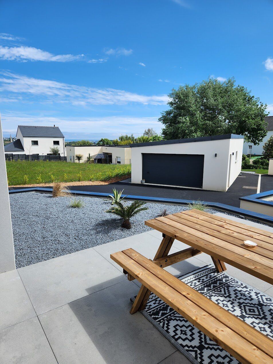 A modern outdoor patio with a wooden table and benches, a swimming pool, and a garage.