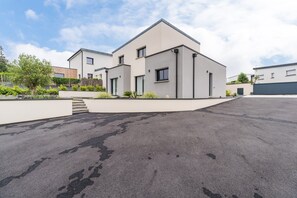 A modern two-story residential building with a flat roof, a driveway, and a landscaped garden area. - Architect-designed house 800m from the sea (Paimpol)