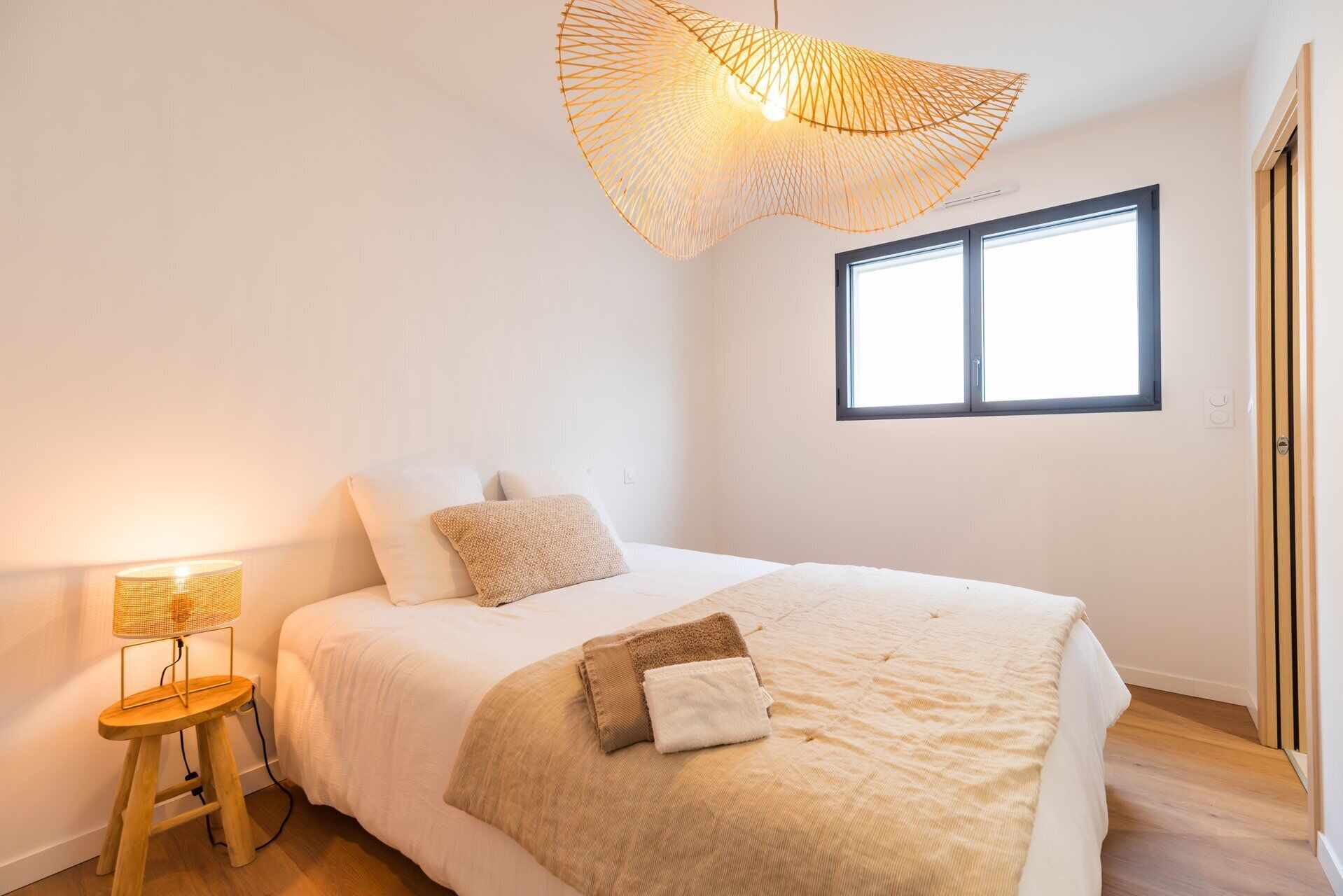 A bedroom with a bed, a standing lamp, a window, and a door.