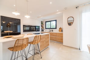 A modern kitchen with a central island, bar stools, and a large window. - Architect-designed house 800m from the sea (Paimpol)
