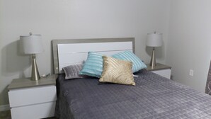Uma cama bem arrumada com um edredom cinza, duas luminárias de cabeceira e uma mesa de cabeceira com uma gaveta.