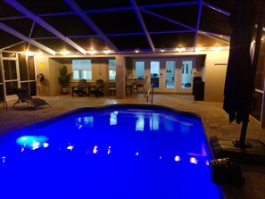Ein Schwimmbad mit einer Deckenkonstruktion, einem Sitzbereich mit Stühlen und einer Essplatz mit Tisch und Stühlen.