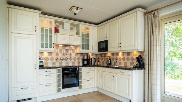 A kitchen with white cabinetry, a microwave, an oven, and a coffee maker. - Texel Nature Villa With Sauna (De Koog)