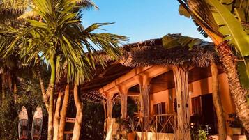 A tropical resort with a thatched-roof structure, palm trees, and a clear blue sky.
