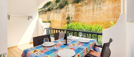 A dining area with a table set for two, a bottle of wine, and a view of a cliff.