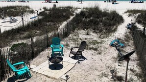 Una playa con una zona arenosa que cuenta con una fogata, sillas y una lámpara solar.