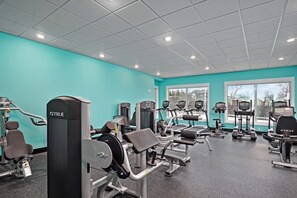 Une salle de sport équipée de divers appareils d’exercice, dotée de grandes fenêtres et d’un mur de couleur turquoise.