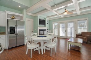 A kitchen with a stainless steel refrigerator, a water dispenser, a white dining table with chairs, and a ceiling fan.
