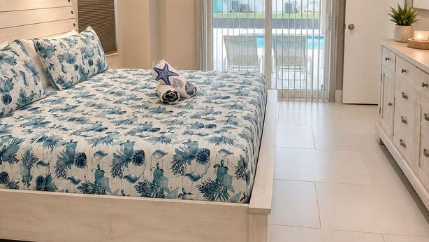 Een slaapkamer met een bed, een plafondventilator, een raam en een deur die uitkomt op een balkon.