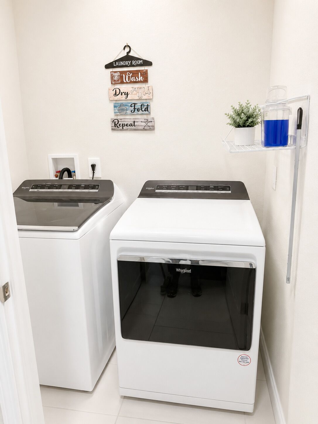 A laundry room with two front-loading washers, a wall-mounted drying rack, and a small potted plant.
