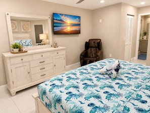 A bedroom with a bed, a massage chair, a TV, and a bathroom visible through an open door.