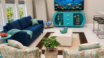 Ein Wohnzimmer mit blauem Sofa, türkisfarbenen Akzentstühlen, einem Flachbildfernseher und einem Deckenventilator.