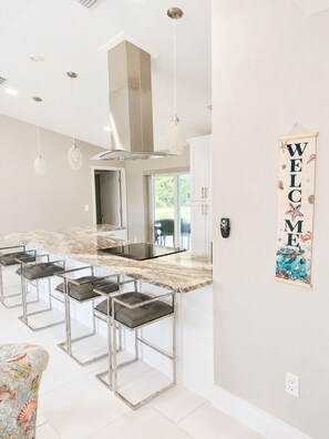 A modern kitchen with a marble countertop, bar stools, pendant lights, and a welcome sign. - Tu hogar lejos de Casa..4BR..POOL ..PET Friendly ! (Port Charlotte)