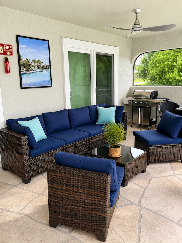 A patio area with a blue sofa set, wicker chairs, a grill, and a fire extinguisher.