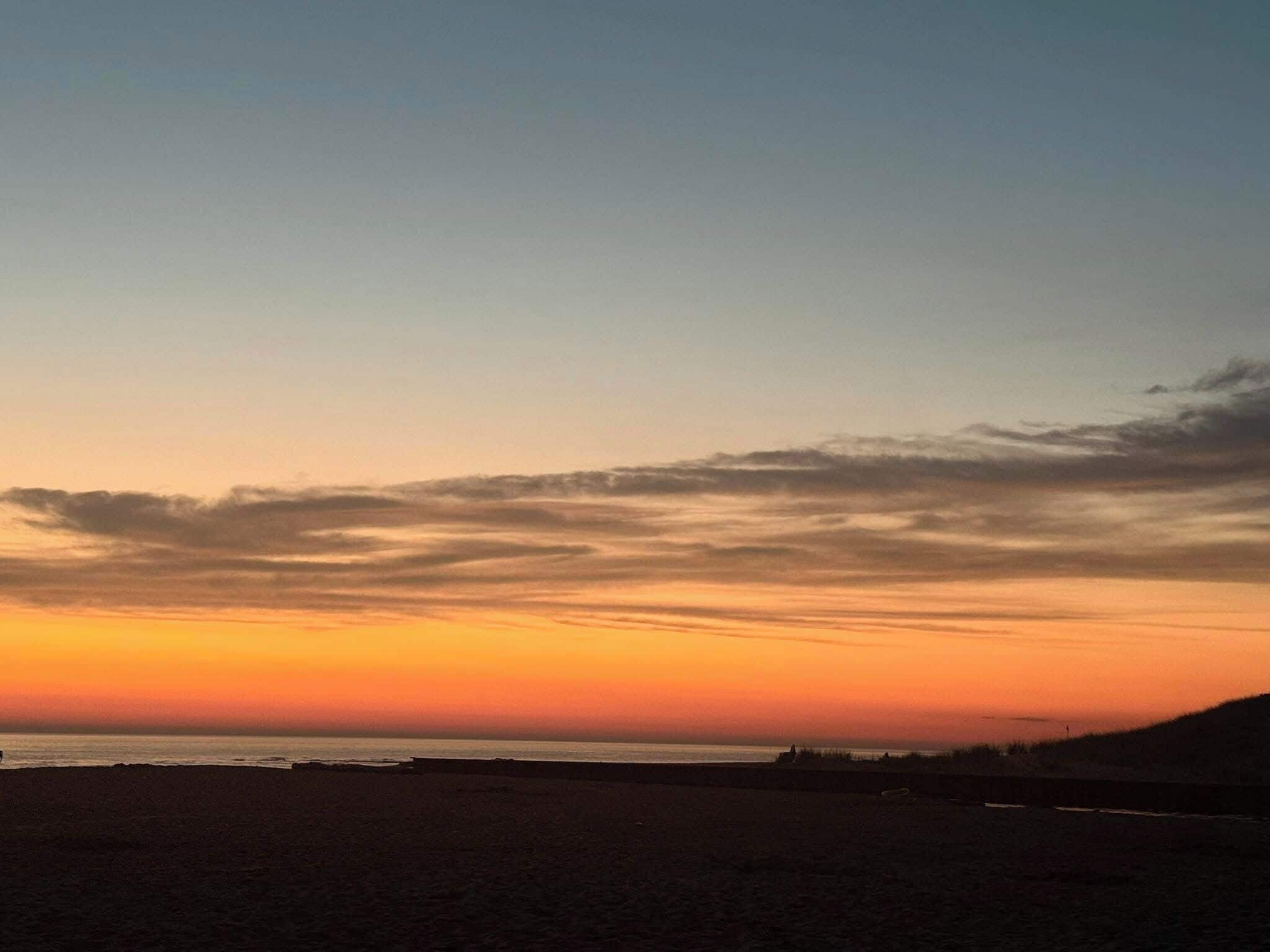 A beach with a sunset sky, calm sea, and distant land.