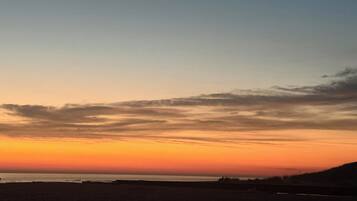 A beach with a sunset sky, calm sea, and distant land.