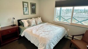 Una camera da letto con un letto, un comodino, una sedia, una finestra con vista e due quadri appesi al muro.