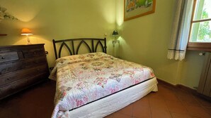 Ein Schlafzimmer mit Bett, Kommode, Lampe, Gemälde und Fenster.
