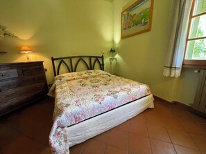 A bedroom with a bed, dresser, lamp, painting, and window. - Casa Magnogia-sotto, cozy apartment with a garden; dogs welcome (Imperia)
