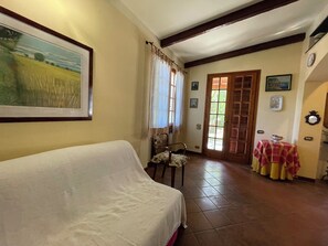 A room with a covered sofa, a dining table with a tablecloth, a chair, a door with glass panels, and a framed picture on the wall. - Casa Magnogia-sotto, cozy apartment with a garden; dogs welcome (Imperia)