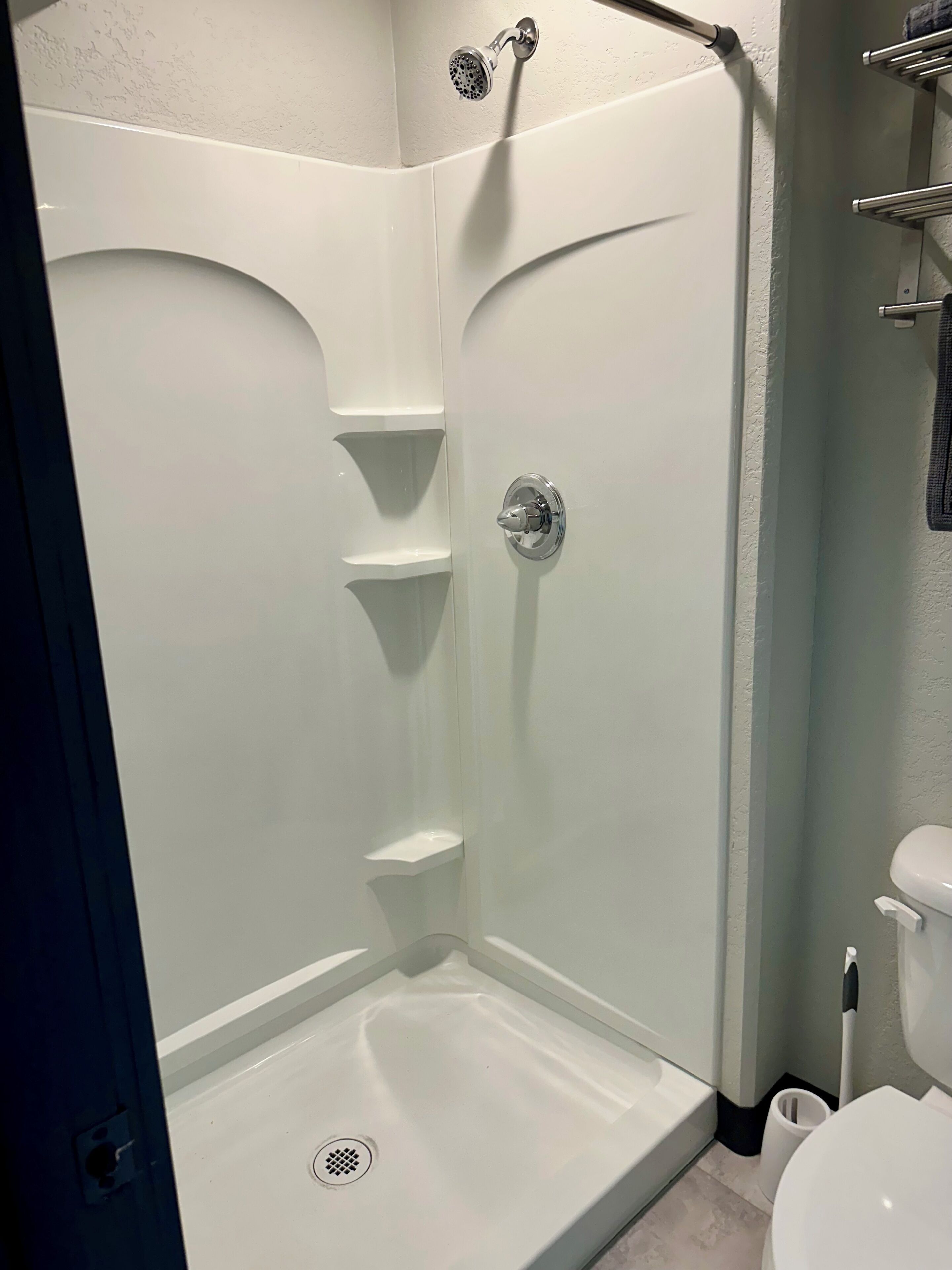 A shower stall with a built-in seat, a handheld showerhead, and a toilet to the right.