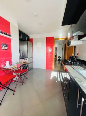 A modern kitchen with red accents, a dining area with red chairs, and a visible kitchen island. - 2 min from Finance City + Fiber + 110 m² + Free Parking + PS4 + IPTV (Casablanca)