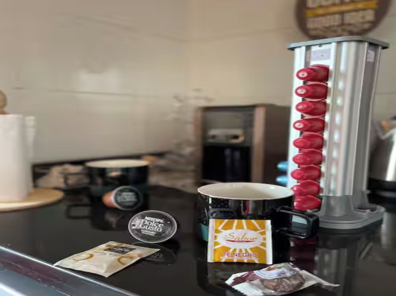 Una cafetera con espumador de leche, un sobre de azúcar y una taza de café sobre una encimera.