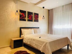 A bedroom with a bed, nightstand, and artwork on the wall. - 2 min from Finance City + Fiber + 110 m² + Free Parking + PS4 + IPTV (Casablanca)
