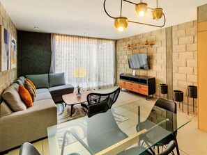 Ein modernes Wohnzimmer mit einem Glastisch, einer Couch, einem an einer Ziegelwand befestigten Fernseher und einem kleinen Couchtisch.
