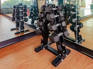Une salle de sport équipée de supports à haltères hexagonaux, d’un plancher en bois et d’un grand miroir qui reflète l’équipement.