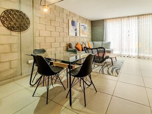 Ein modernes Wohnzimmer mit einem Glastisch, schwarzen Stühlen, einem grauen Sofa und einem gemusterten Teppich.