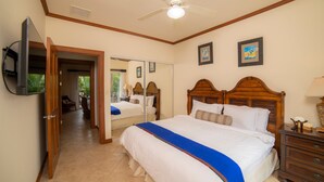Une chambre d’hôtel avec un lit, un ventilateur de plafond, un téléviseur fixé au mur et une table de chevet en bois.