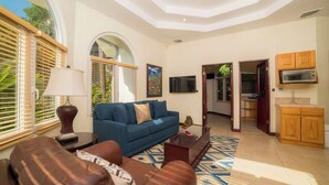 A living room with a blue sofa, a brown leather couch, a lamp, and a TV. - Harmon House 6 BR with private pool (Playa Herradura)