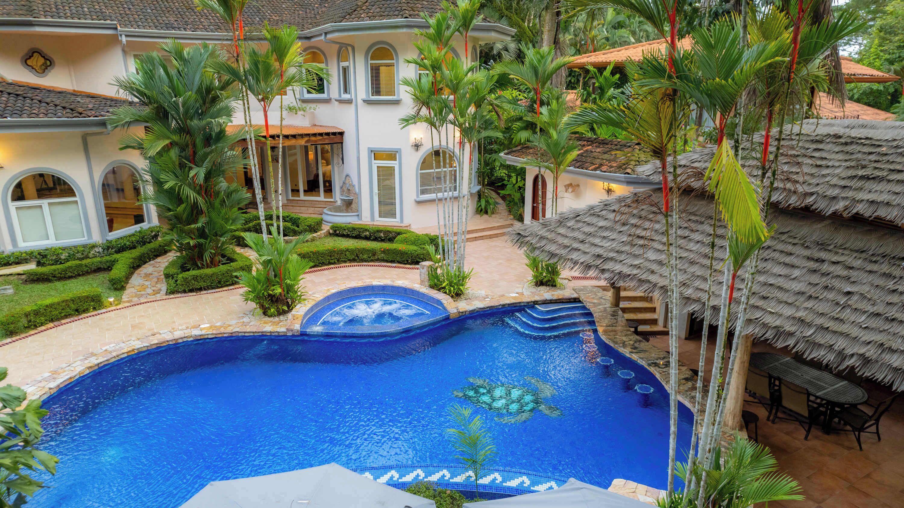 Une grande piscine entourée de plantes tropicales et un bâtiment doté d’un toit en tuiles.