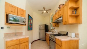 A compact kitchen with wooden cabinets, a microwave, a refrigerator, a stove, and a ceiling fan. - Harmon House 6 BR with private pool (Playa Herradura)