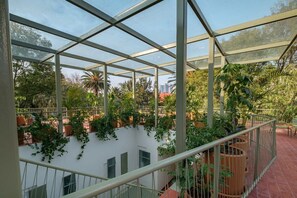 A covered outdoor area with a glass ceiling, surrounded by potted plants and a white building with windows. - CAM 1-Bedroom Deluxe (Ciudad de México)