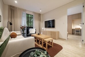 A modern living room with a sofa, a coffee table, a TV mounted on the wall, and a dining area with a table and chairs. - CAM 1-Bedroom Deluxe (Ciudad de México)