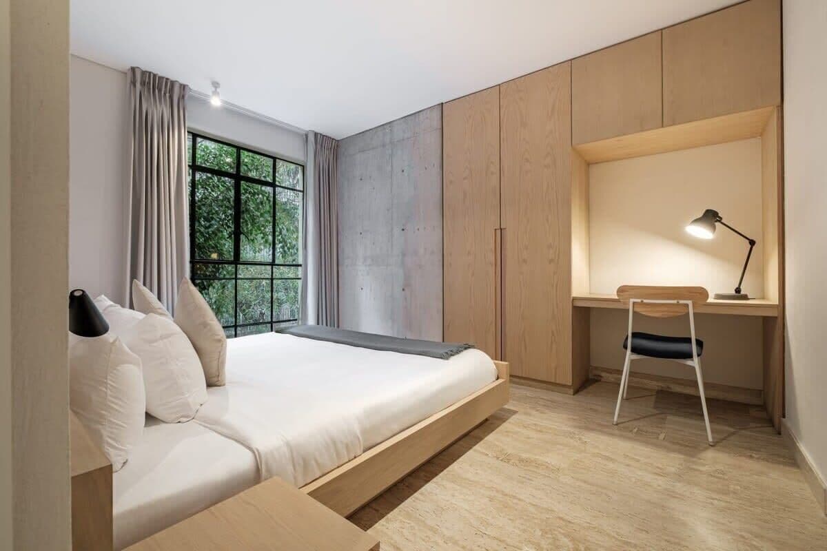 A bedroom with a bed, a desk, a chair, and a window with curtains.