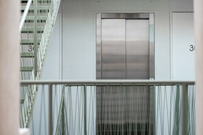 A modern elevator with a metallic finish, flanked by white walls and a metal railing. - CAM 1-Bedroom Deluxe (Ciudad de México)